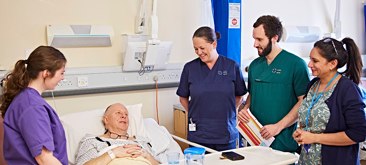 Four health professionals looking over male patient in hosptal bed 