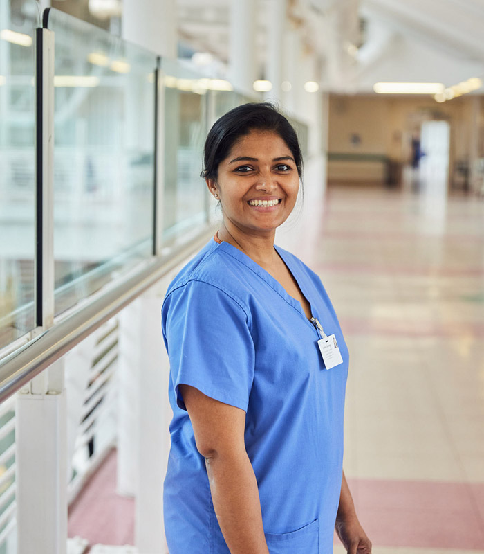 Scrub nurse looking and smiling at the camera, with hospital corridor in the background 