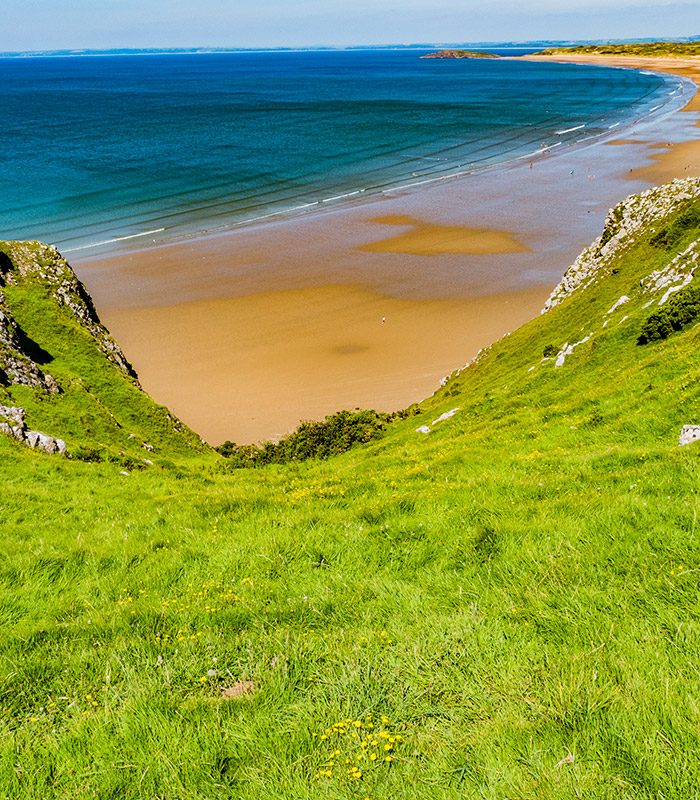 In the foreground we see the rolling hills, in the background a sandy beach and the sea 
