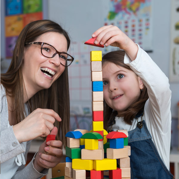 Female child building block tower with woman who is smiling 