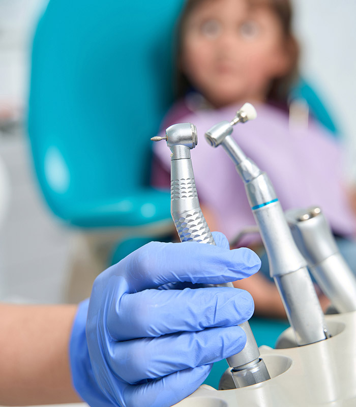 Hand holding dentist tool with blurred child in dentist chair in the background