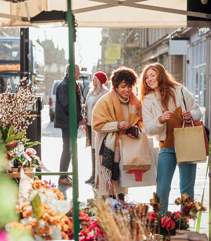 Two women walking along chatting while at a flower market 