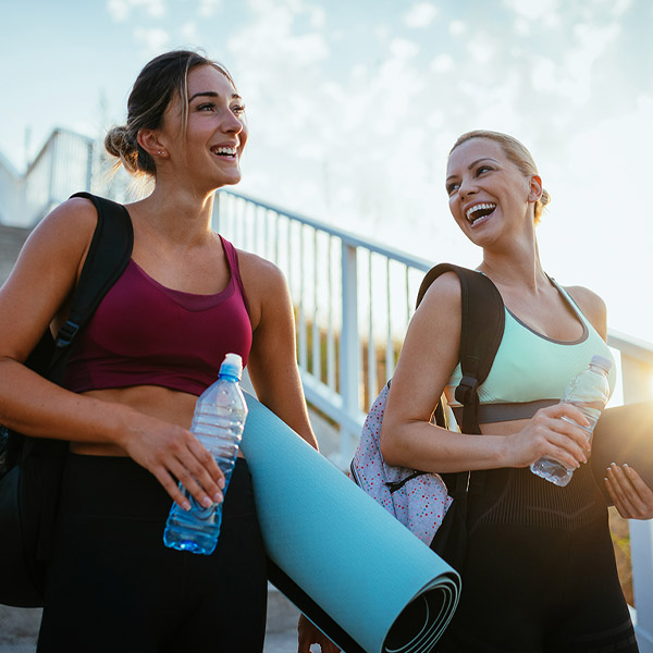 Two women smiling walking with yoga mats in hand 
