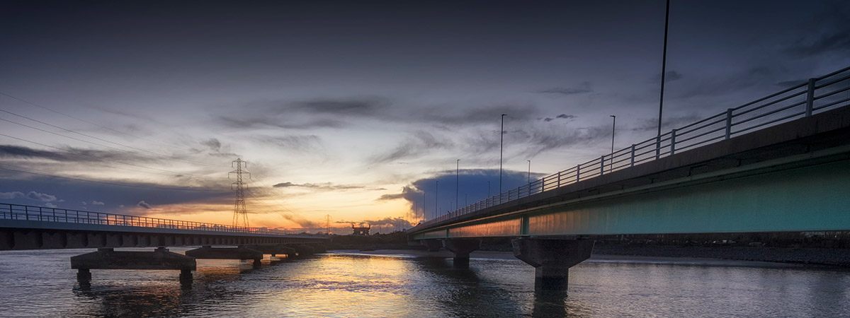 Panorramic shot of a bridge which goes into the distance, with the sun setting in the foreground 