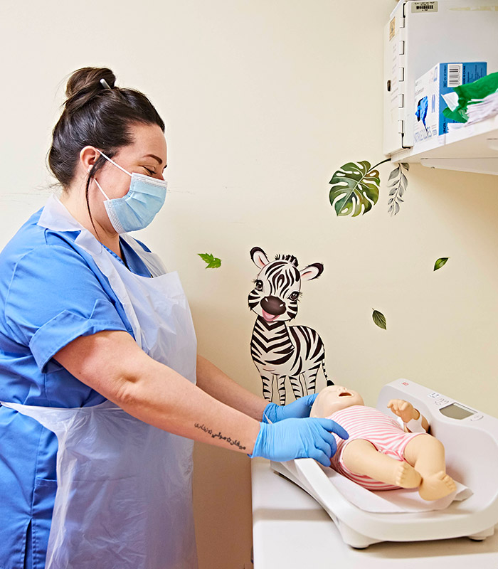 Woman nurse wearing surgical mask looking at doll baby on a changing table