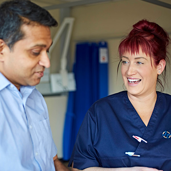 Woman nurse smiling at male colleague who is looking down at something out of frame