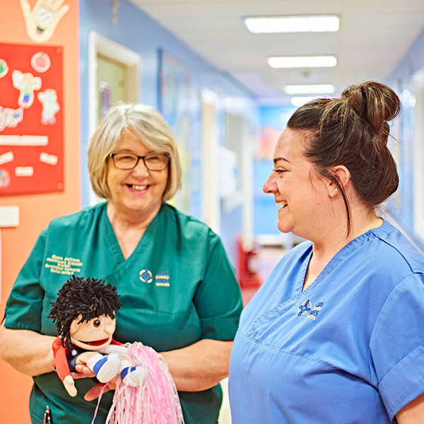 Woman nurse smiling with female colleague, holding a puppet 