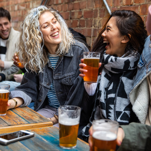 Two women smiling while having a drink at a pub garden 