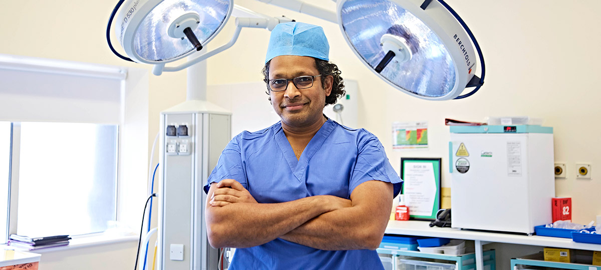 Man in surgeon uniform smiling at camera with arms crossed 